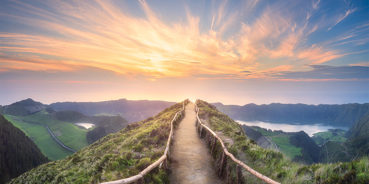 Path with wooden railings along the top of a hill going into the sunset